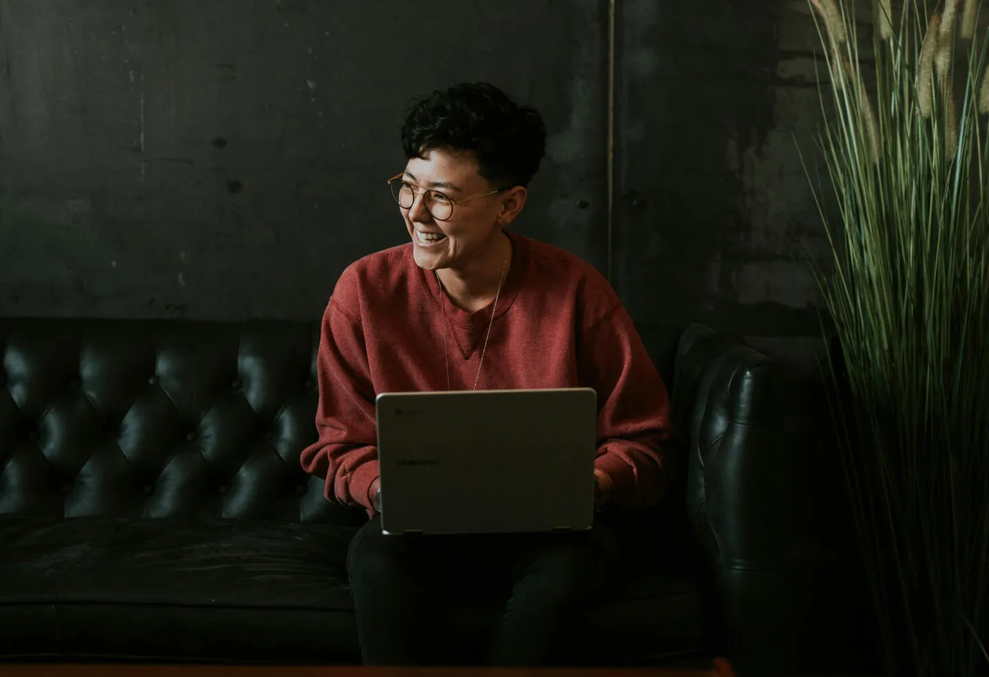 A smiling person using a laptop on a leather sofa