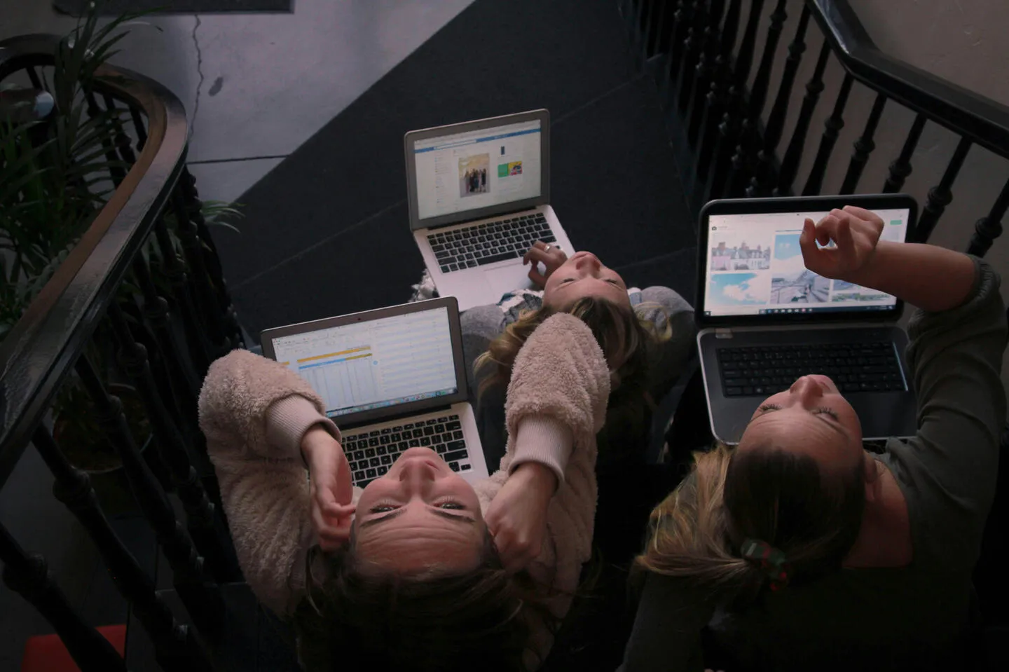 Three women working on laptops together on a staircase